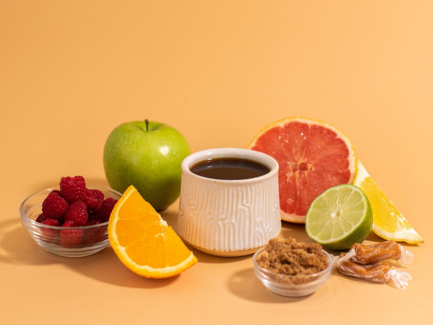 a coffee cup surrounded by fruit, caramels, and sugar