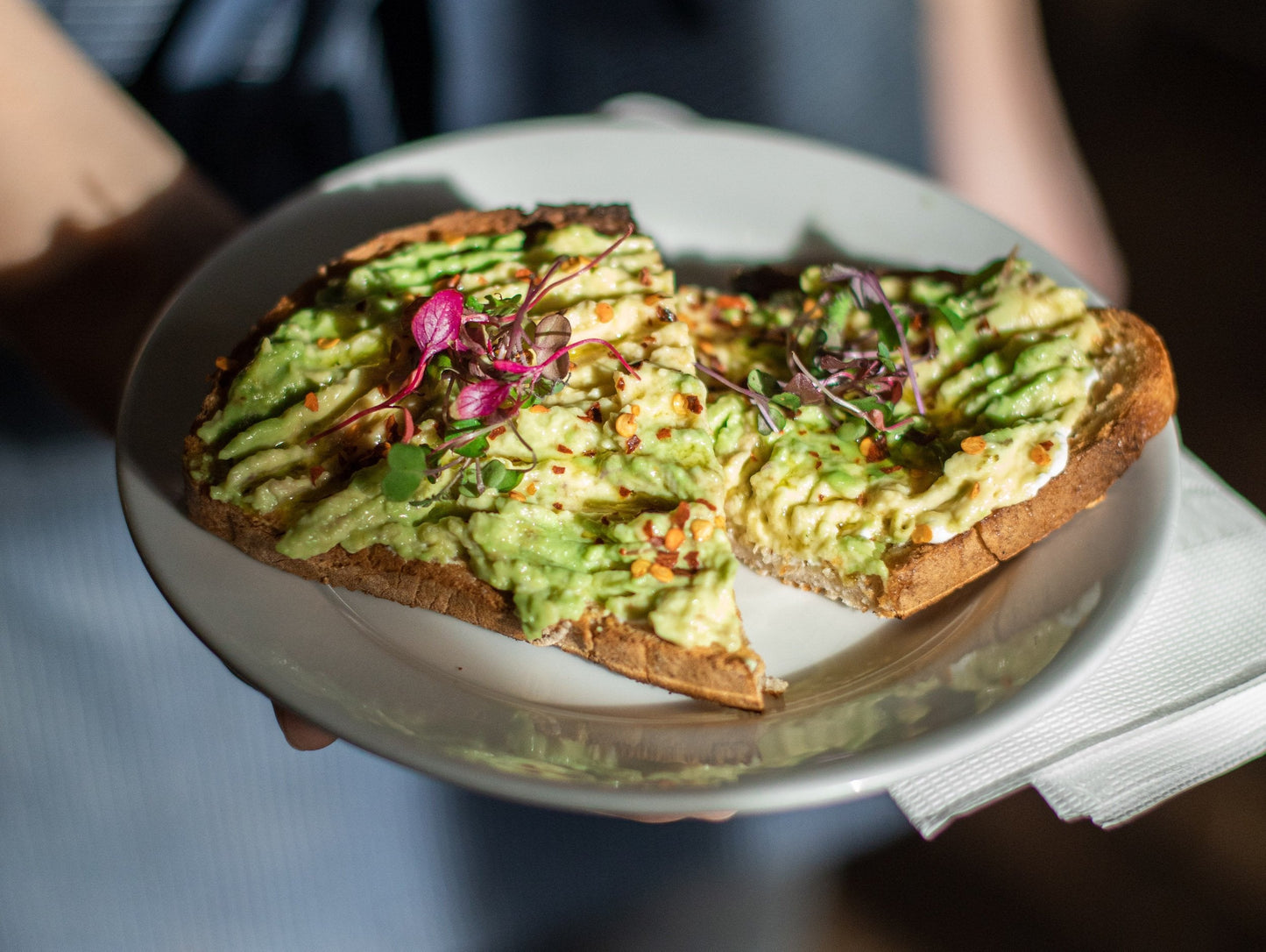 avocado toast cut in half on a white plate being held