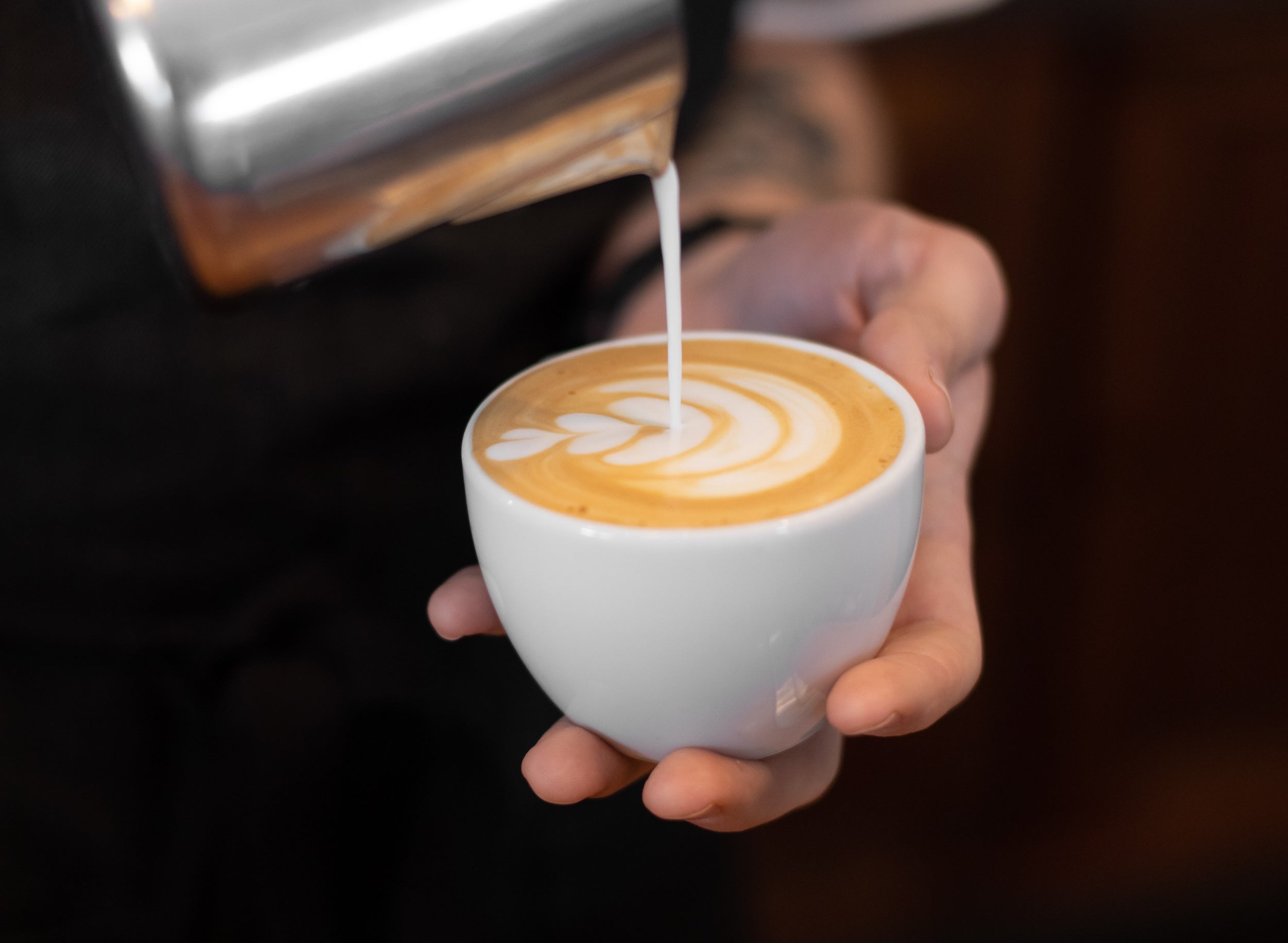 milk being poured into a small latte mug with latte art