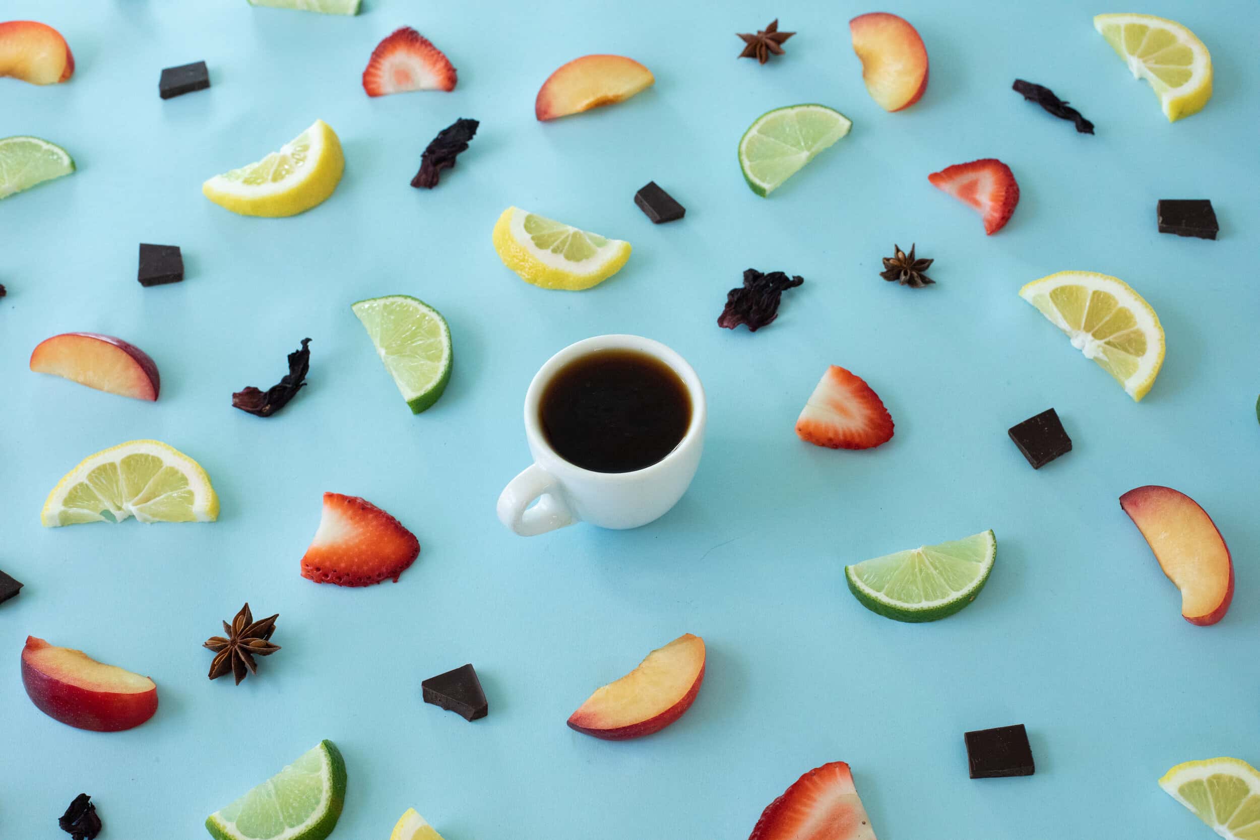 a white cup of coffee on blue background surrounded by sliced fruits